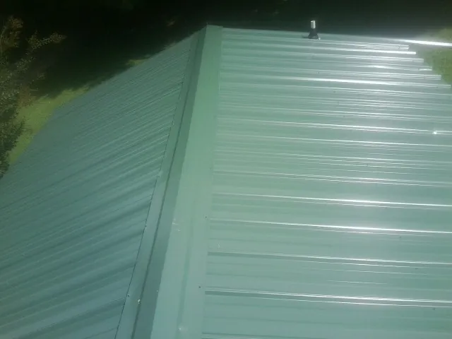 New green metal panels meeting at the ridge of a roof — Flat Roof Repair work by our crew in Ashland